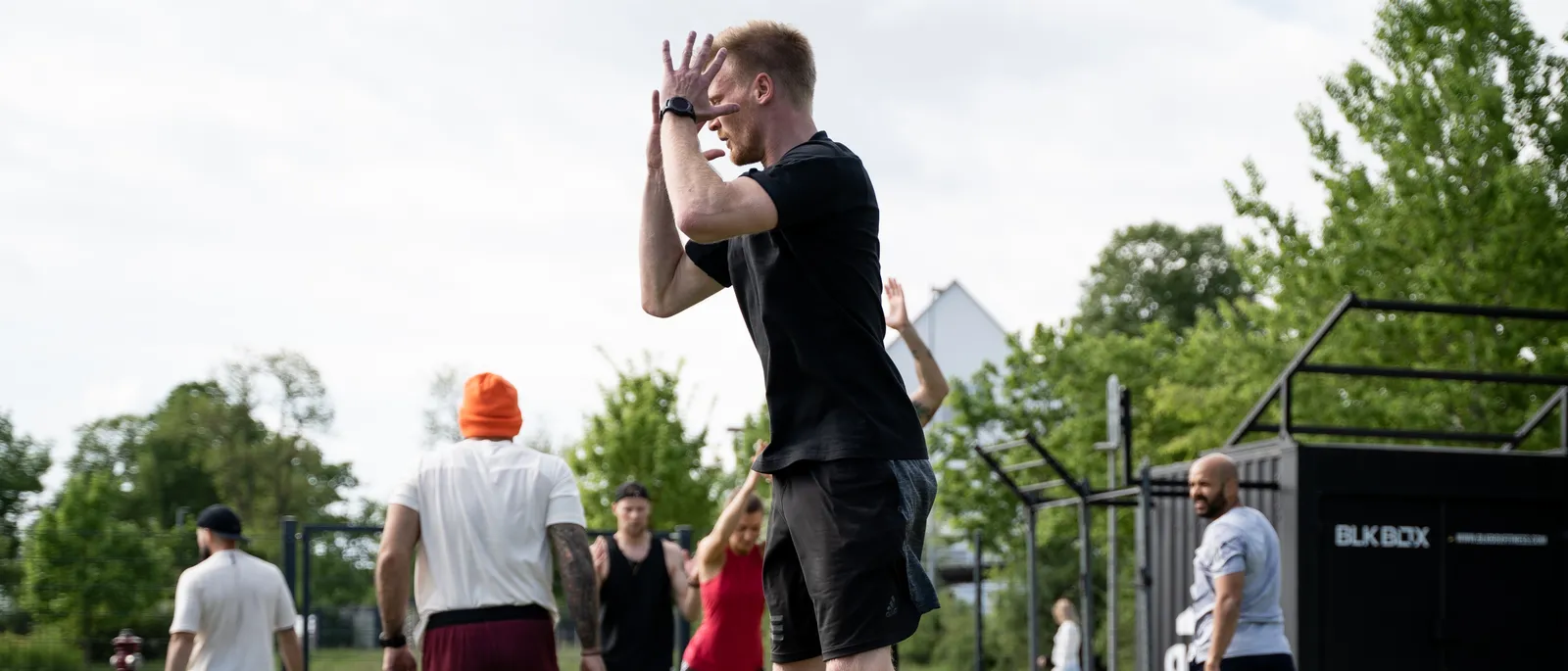Daniel Hense springt auf dem Kunstrasen explosiv nach oben, im Hintergrund wärmt sich eine Trainingsgruppe zwischen gelben Minihürden auf